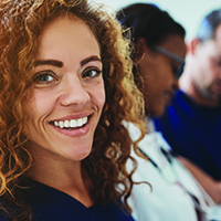 a nurse smiling at the camera while two coworker review documents in the background